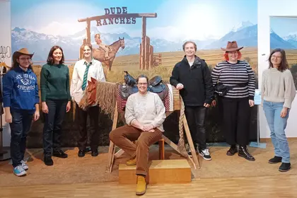 group of students pose in front of scenic image of a dude ranch gate