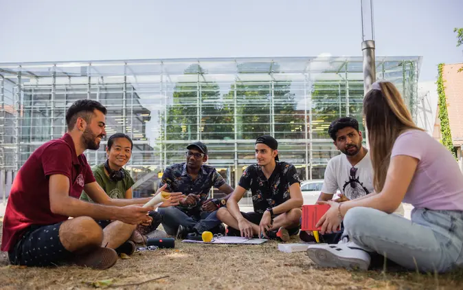 Studierende sitzen vor der Teilbibliothek 4 und diskutieren.